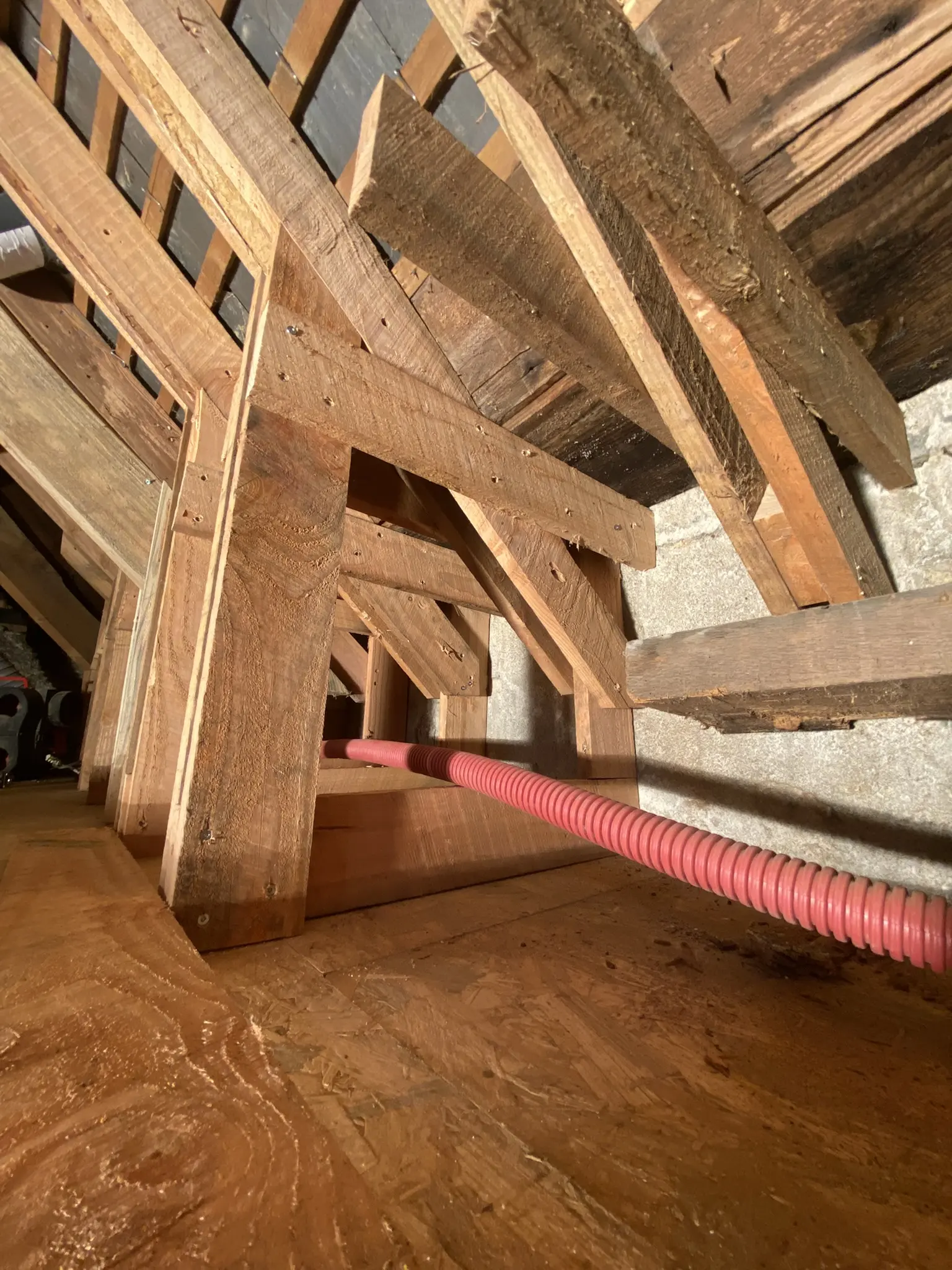 Structure de charpente en bois avec une goulotte rouge passant à travers les poutres dans un espace intérieur.