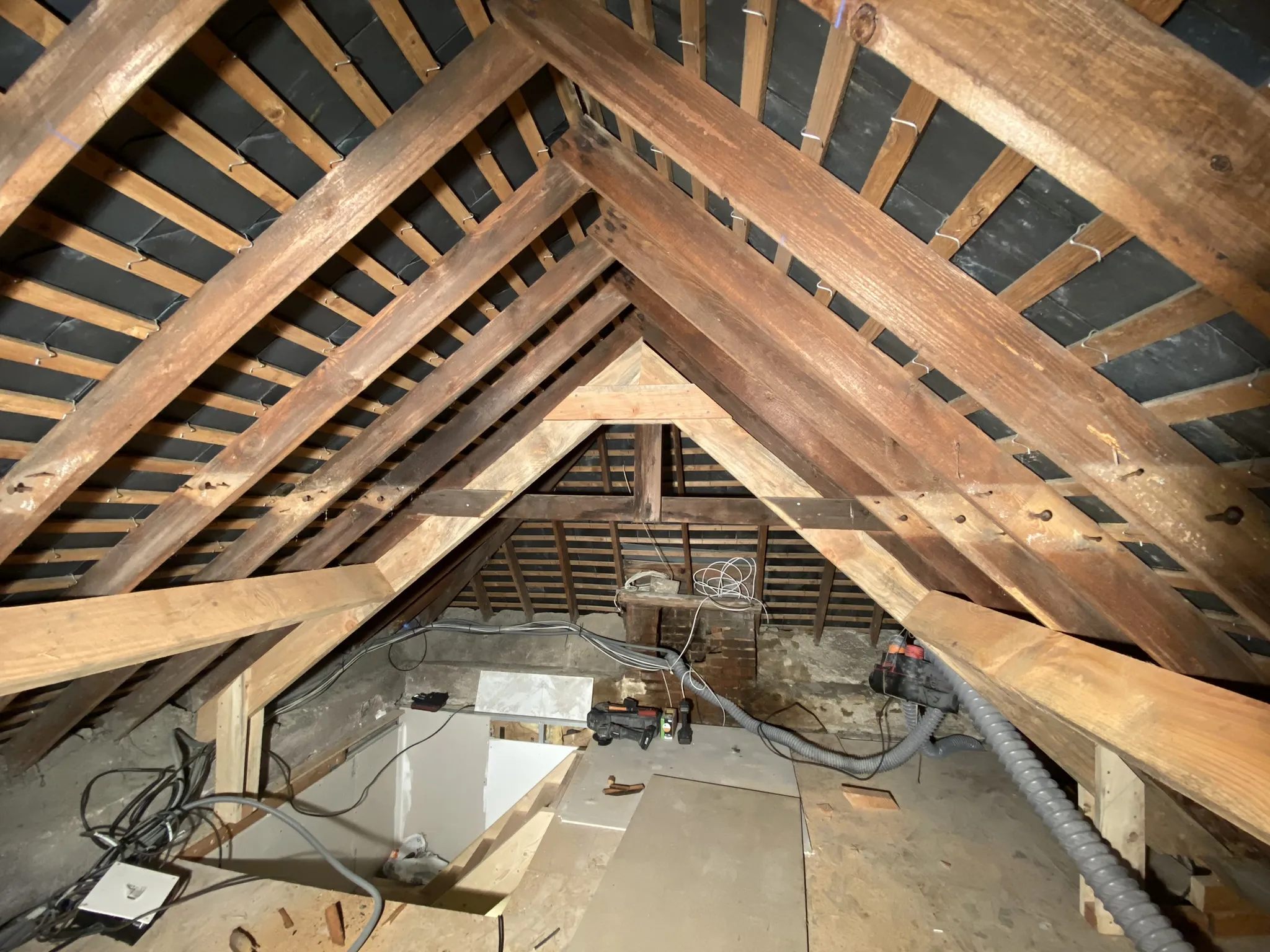 Vue intérieure d'un comble non aménagé avec une charpente en bois et des câbles électriques apparents