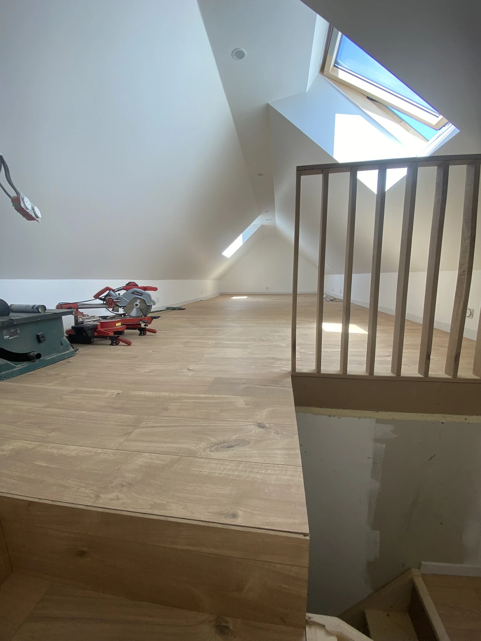 Combles avec plancher en bois clair, fenêtre de toit, outils de bricolage et rampe d'escalier en bois