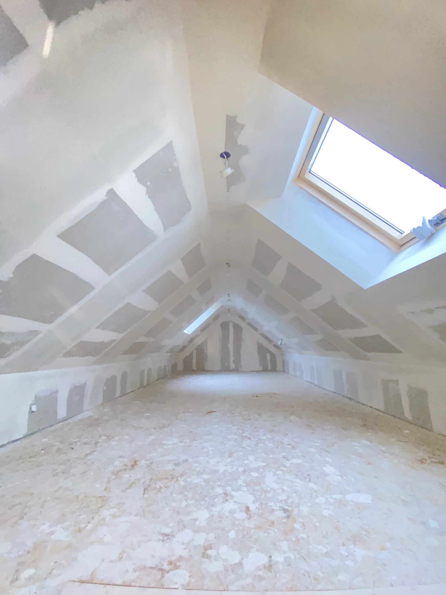 Combles non aménagés avec plaques de plâtre posées sur les murs et plafond, sol brut, fenêtre de toit ouverte