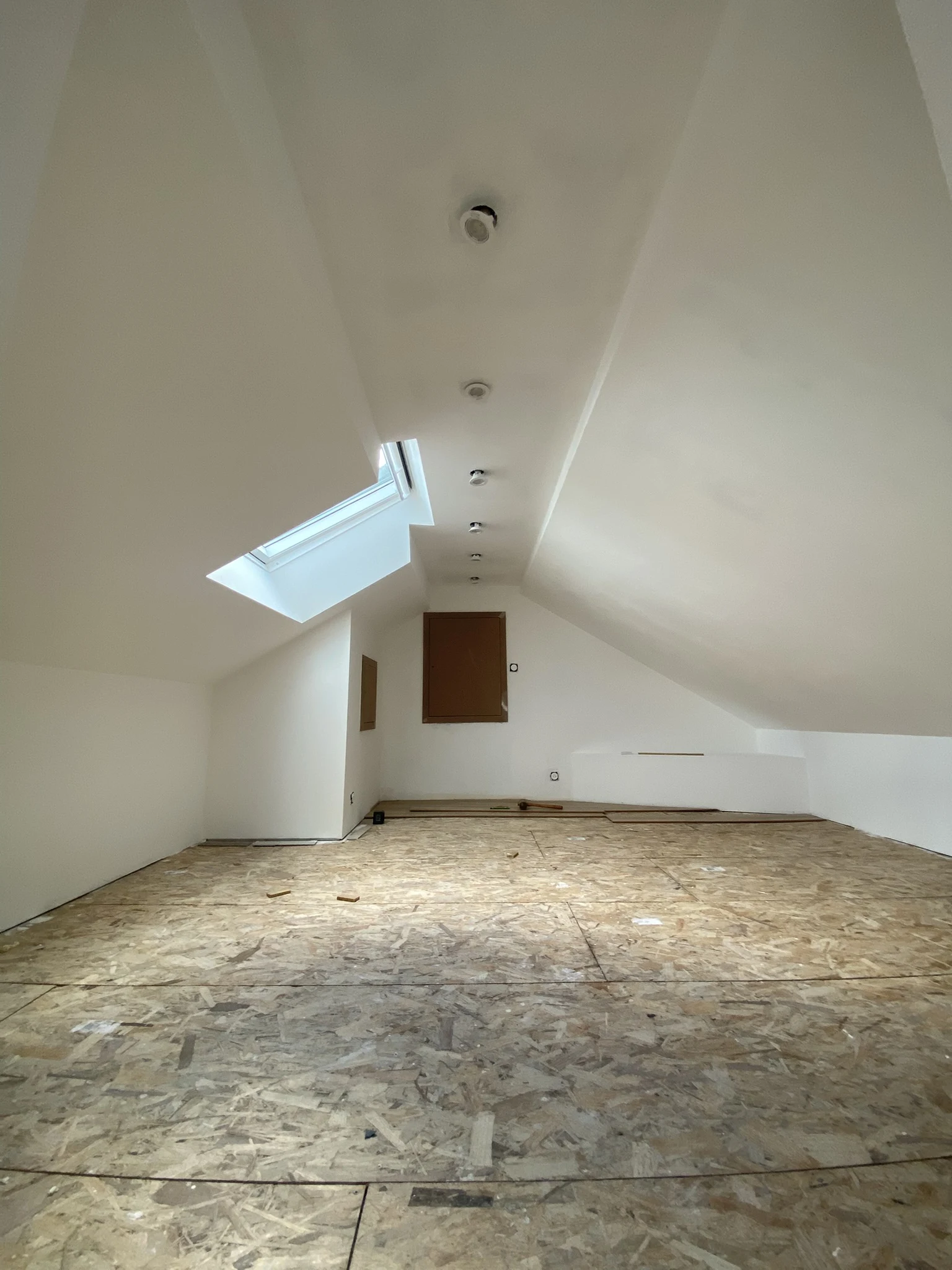 Combles rénovés avec plancher en panneaux OSB, murs et plafond blancs, fenêtre de toit et plusieurs détecteurs au plafond