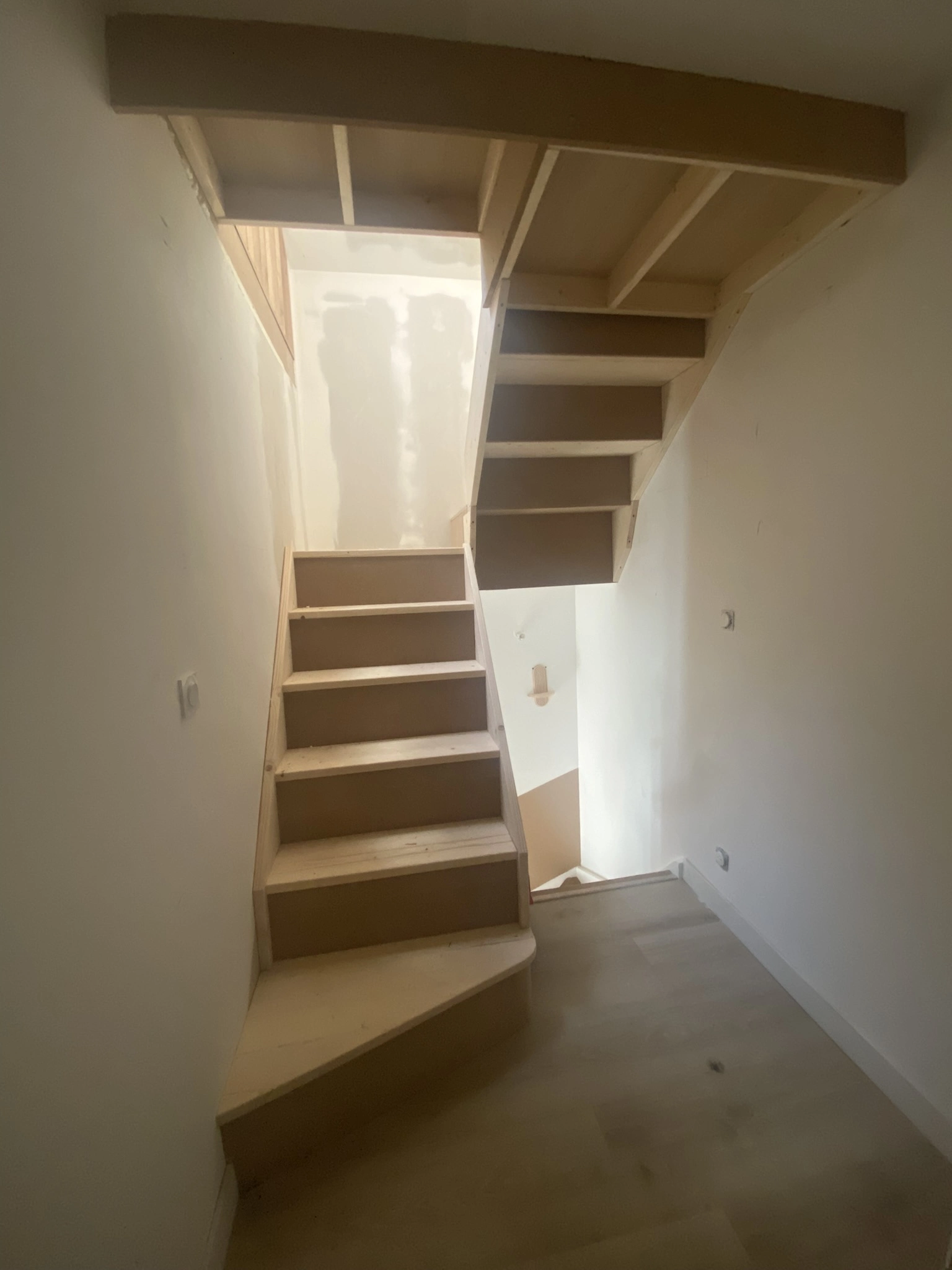 Escalier en bois clair à l'intérieur d'une maison en cours de construction ou de rénovation, murs blancs non finis