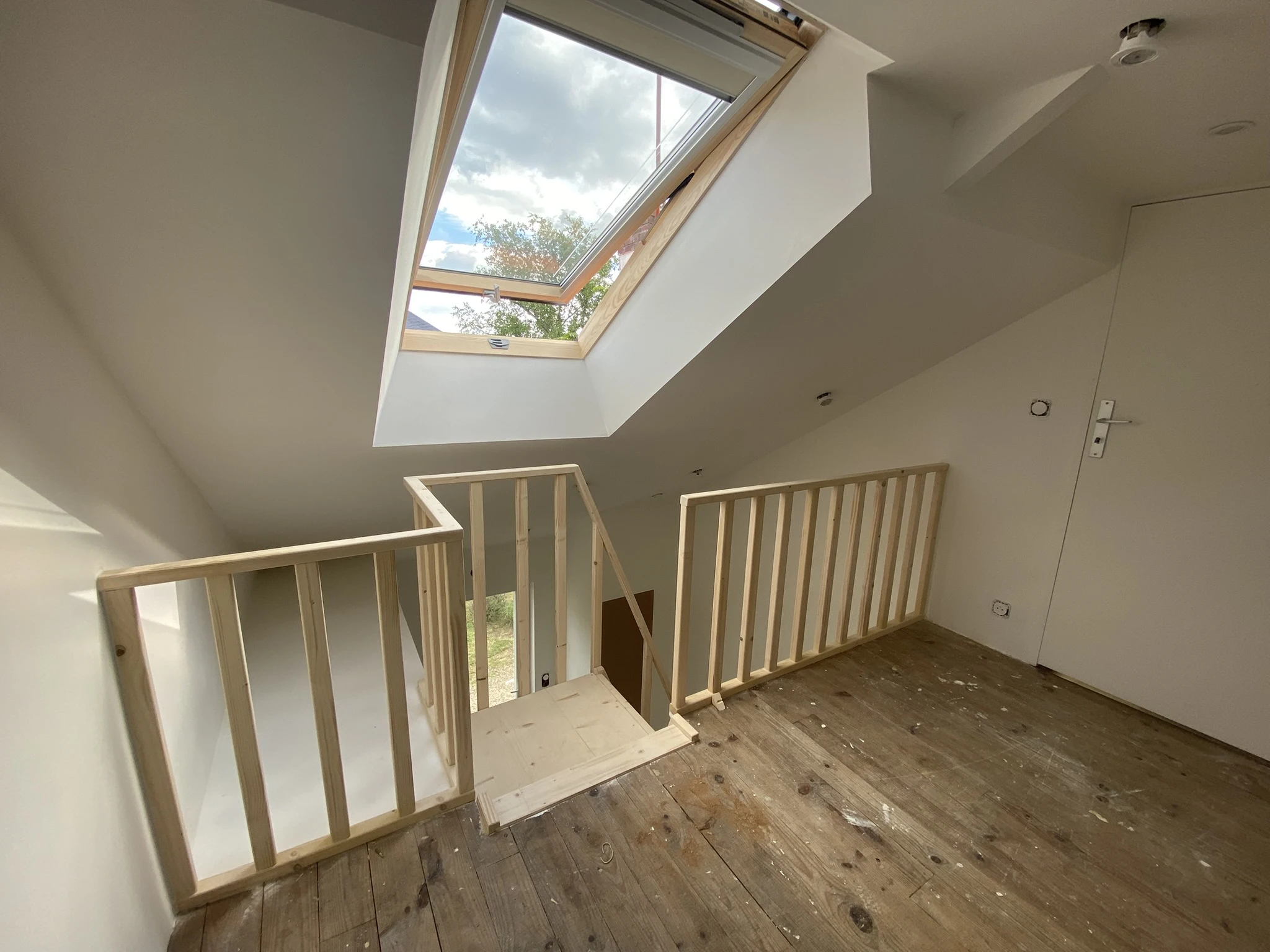 Escalier en bois sous comble avec rambarde en bois clair et fenêtre de toit ouverte laissant entrer la lumière naturelle
