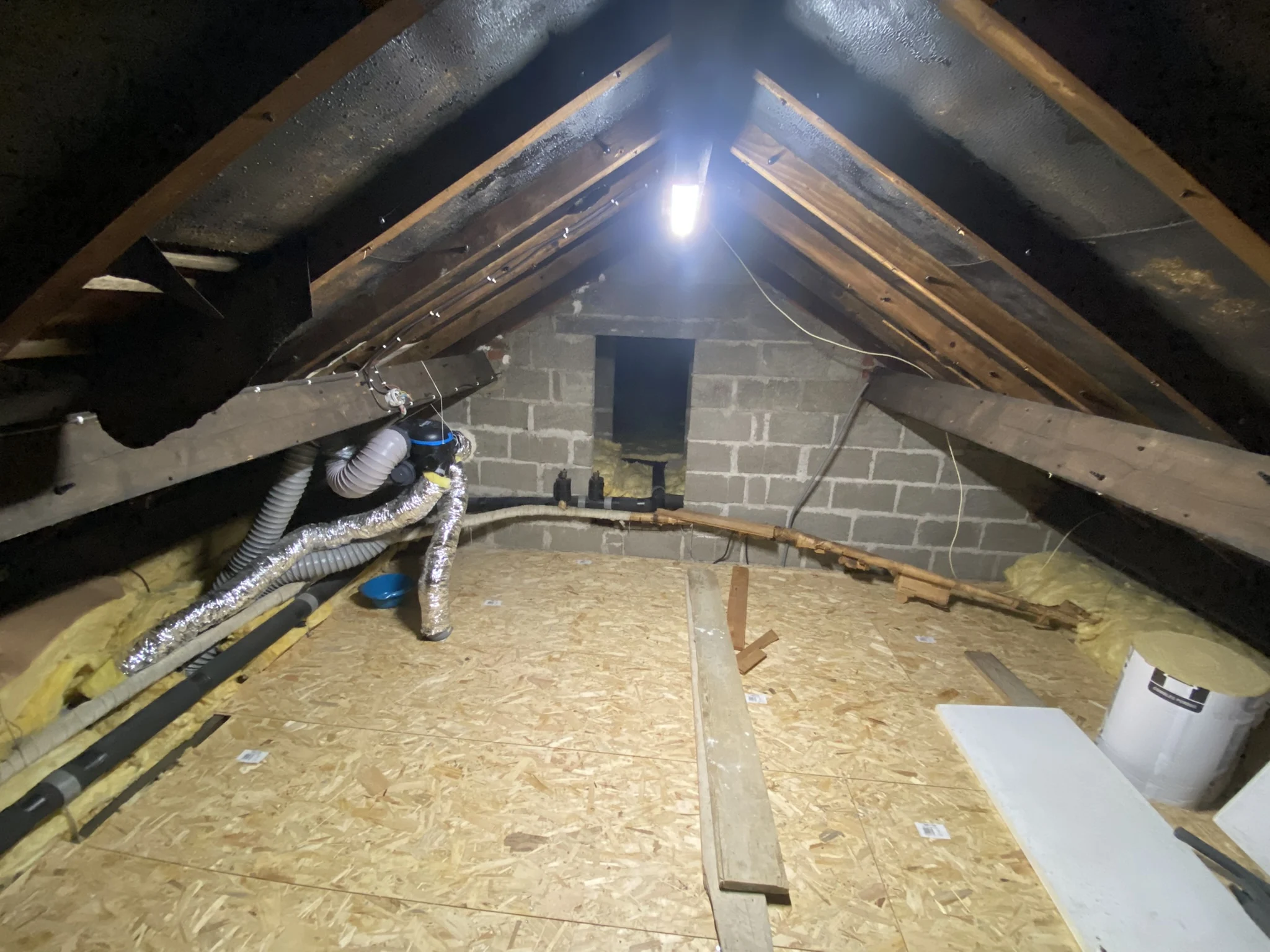 Grenier avec isolation, conduits d'aération, planches de bois et lumière suspendue au plafond