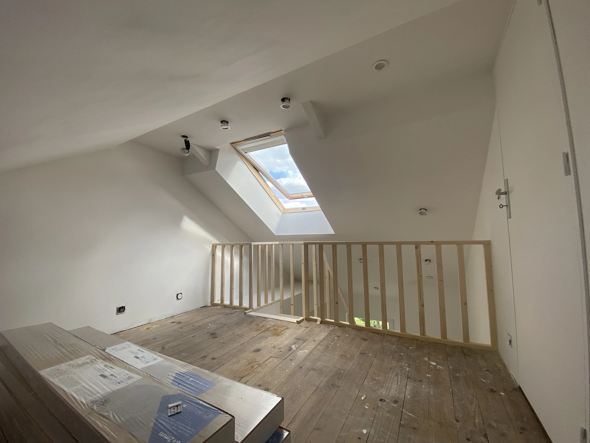 Intérieur d'un grenier avec plancher en bois, rambarde en bois clair et fenêtre de toit laissant entrer la lumière naturelle