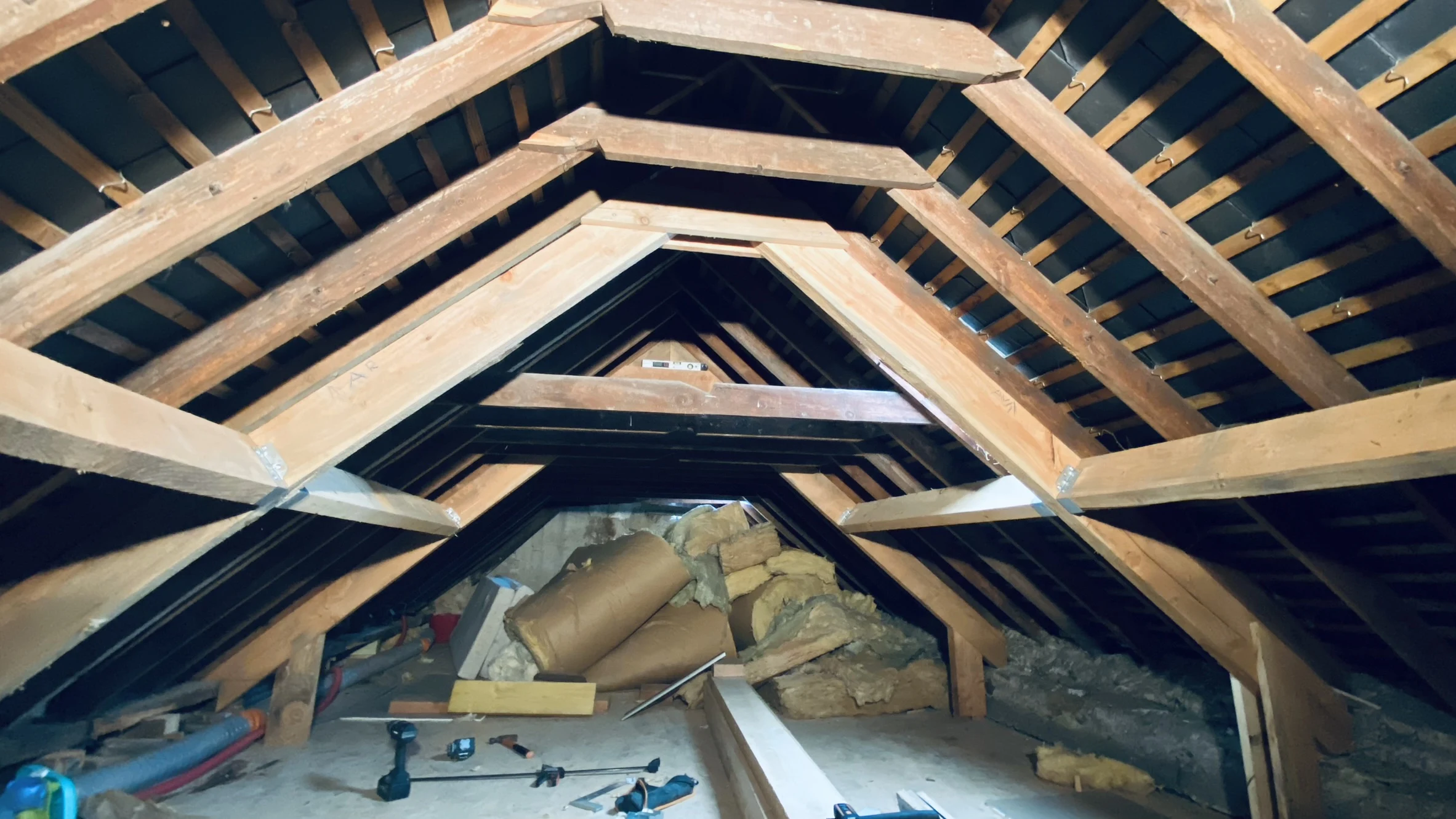 Intérieur d'un grenier avec charpente en bois et matériaux d'isolation posés au sol