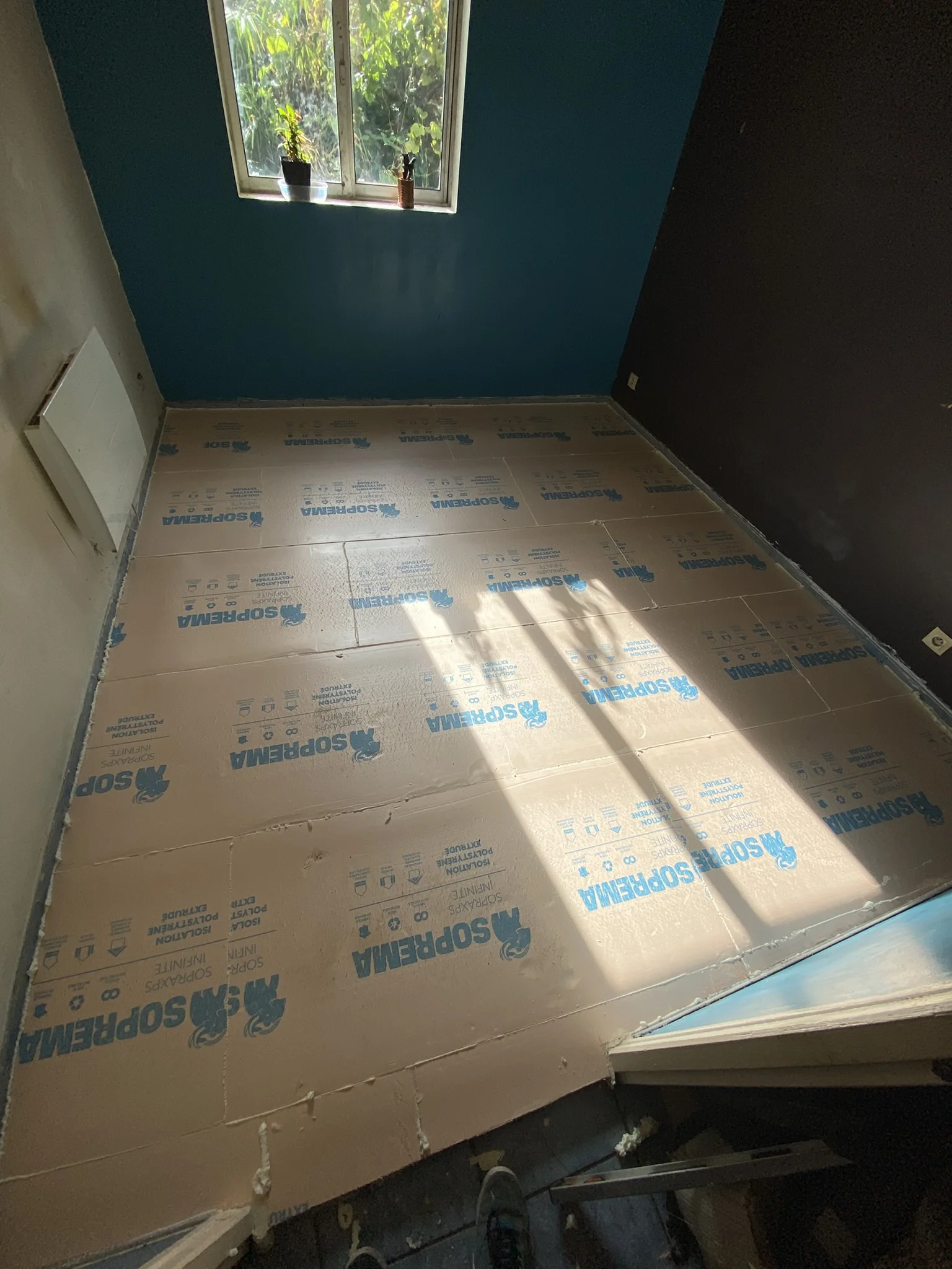 Chambre avec isolant rigide Soprema posé au sol devant une fenêtre avec deux plantes.