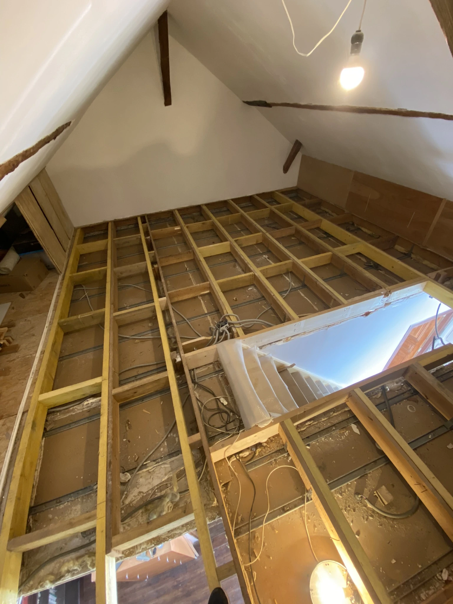 Vue d'un plancher de combles en cours de rénovation avec des solives en bois apparentes et des câbles électriques visibles
